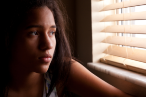 Teen or tween girl struggling with mental illness looks sad as she gazes out a window.