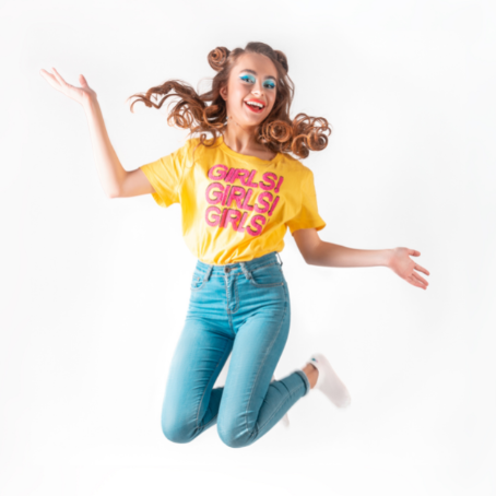 Tween or teen girl jumps up in celebration wearing a bright shirt that reads, "Girls! Girls! Girls!"
