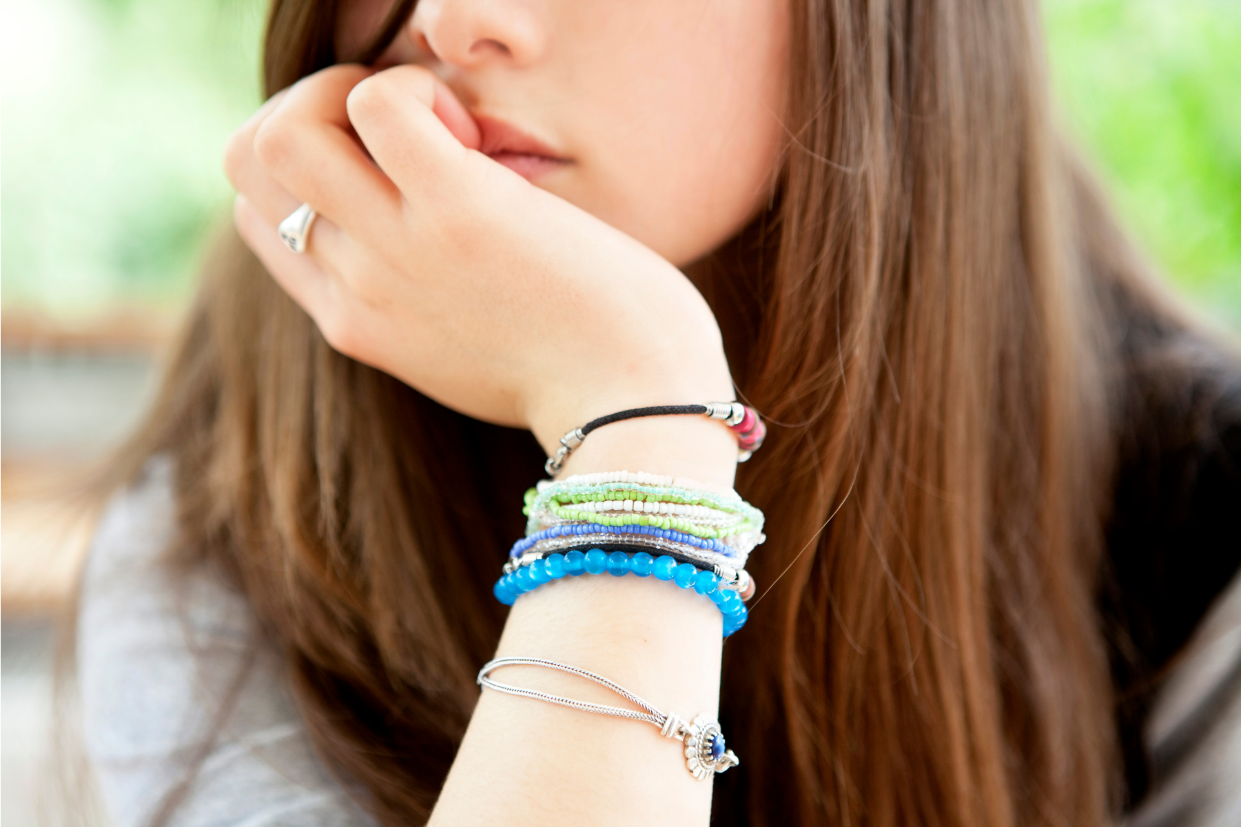 Tween or teen girl wearing bracelets sits bored with her chin in her hand.
