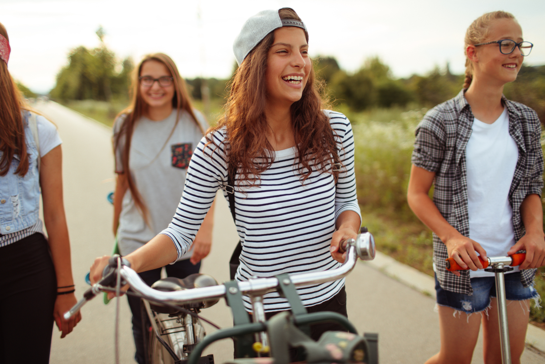 Tween and teen girls walk bikes and scooters down a neighborhood street