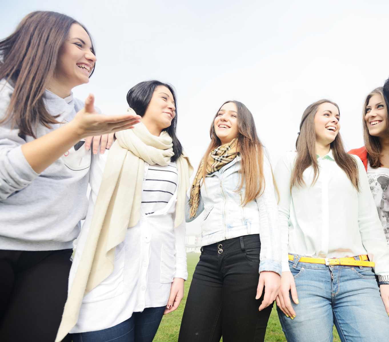 A group of popular tween and teen girls gather outside and laugh.