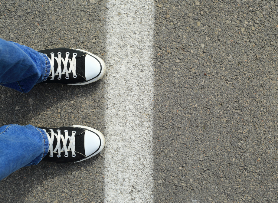 A tween or teen girl stands wearing jeans and black converse shoes with her toes on a white boundaries line.