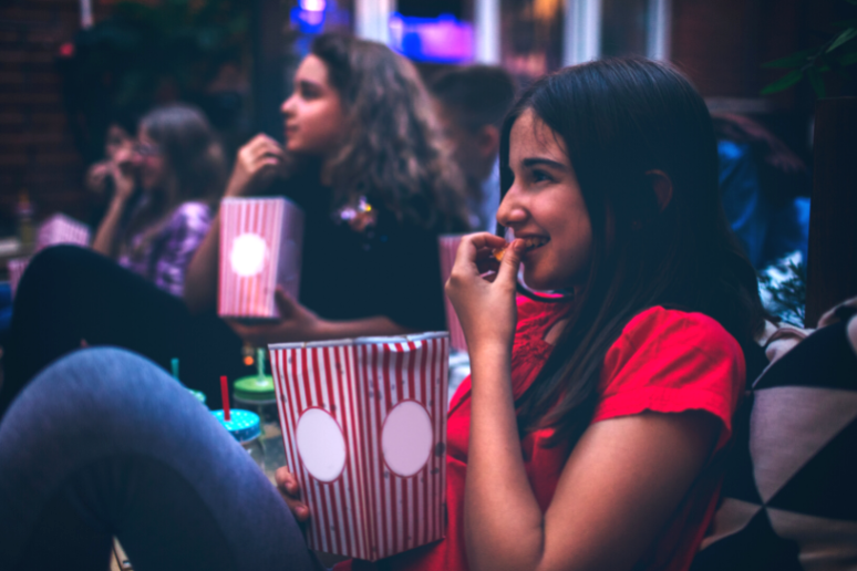 Teen and tween girls watch a movie while eating popcorn.