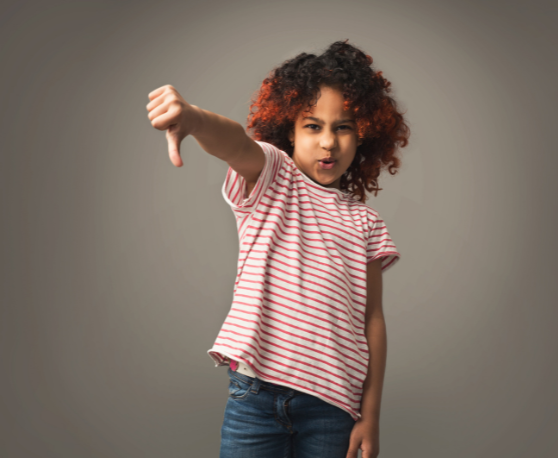 A tween or teen girl with brown skin and curly black hair with red tips says no while holding her thumb down.