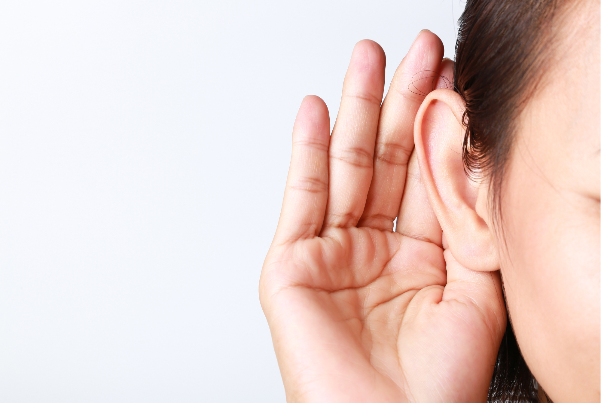 A tween or tween girl with tan skin and dark hair puts her hand behind her ear to listen better.