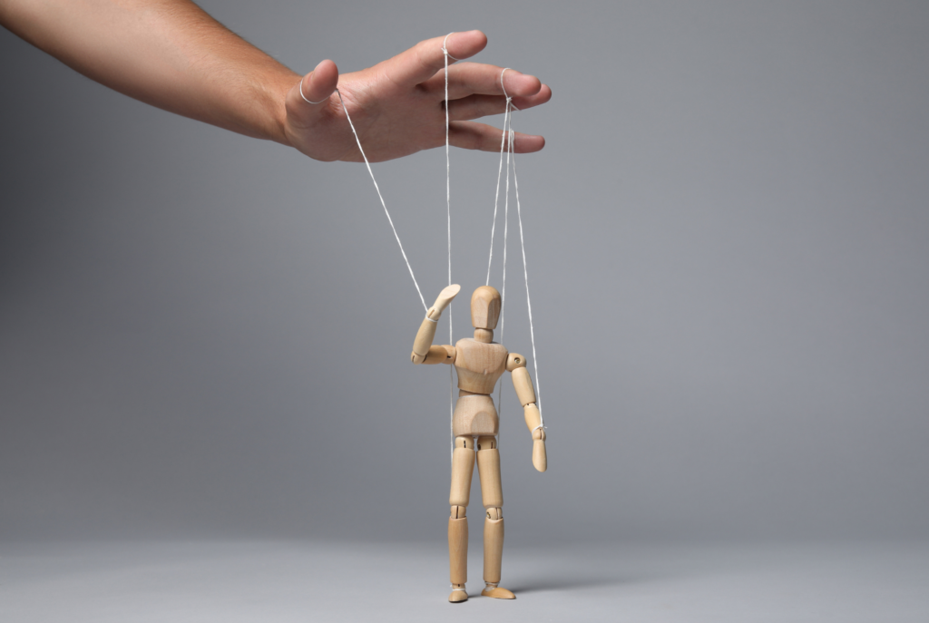 A puppet is controlled by strings attached to a hand hovering above it, symbolic of unhealthy relationships with red flags.