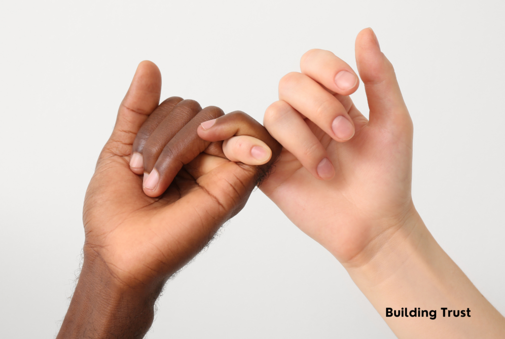 Two tween and teen girls' hands are shown linking pinkies in trust. One girl has darker skin and the other has fair skin.