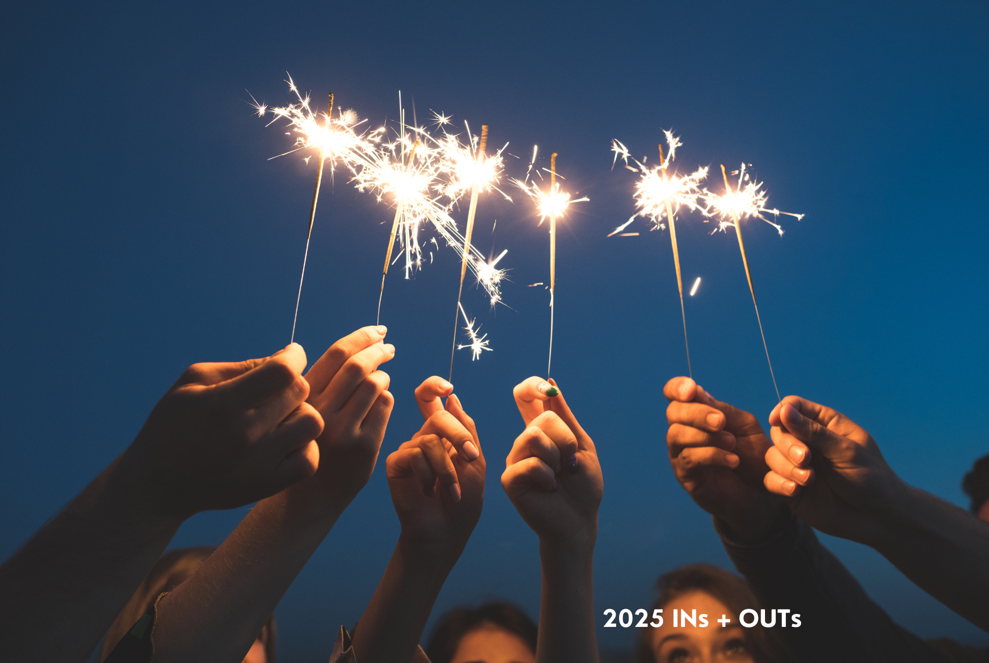 A group of teen or tween girls hold up lit sparklers against a dark sky while thinking of their INs and OUTs for 2025.