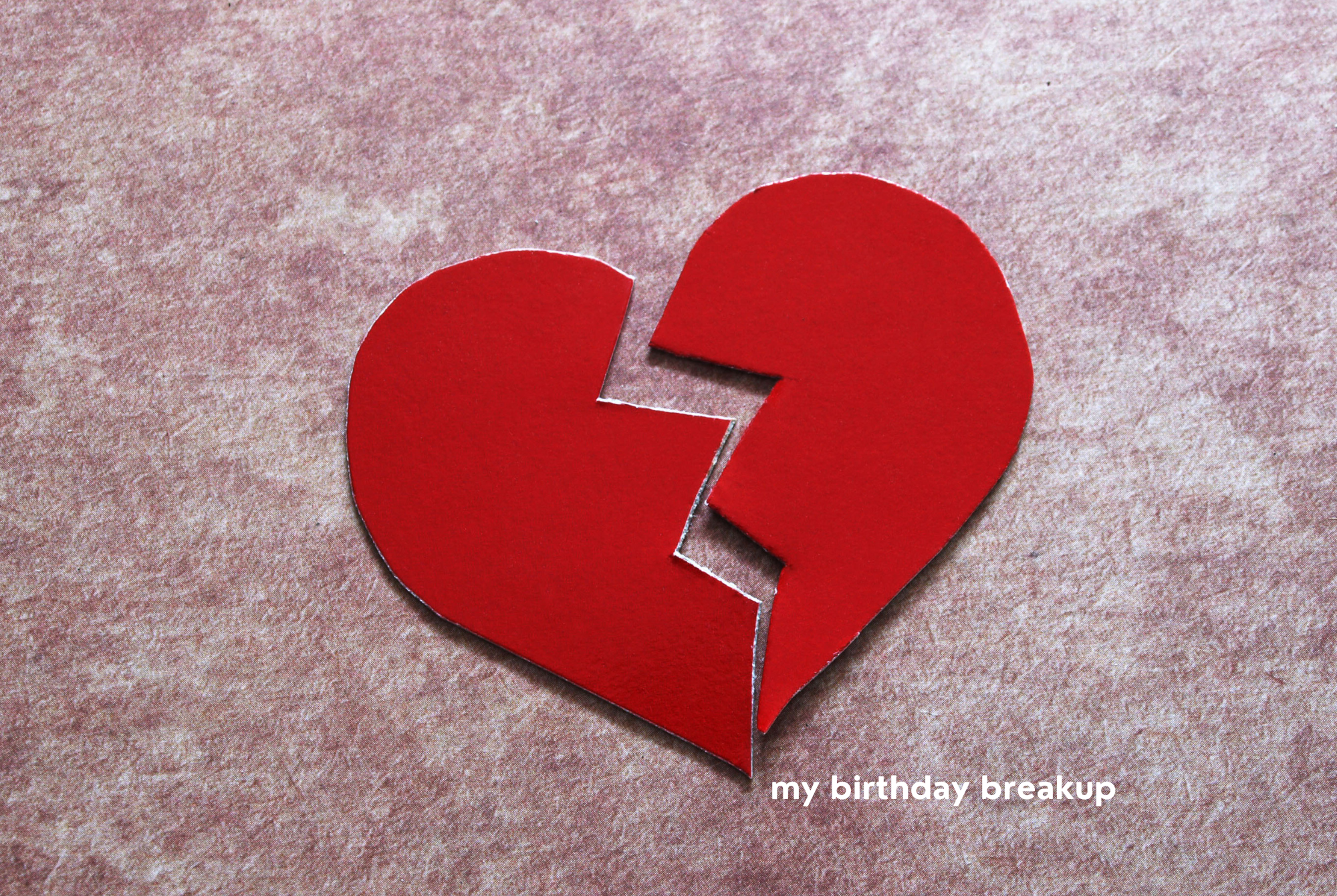 A paper heart lays broken on a soft pink background.