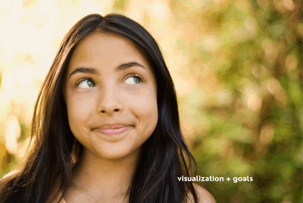 A teen or tween girl with tan skin and long, straight brown hair stands outside in the sun, visualizing her goals.