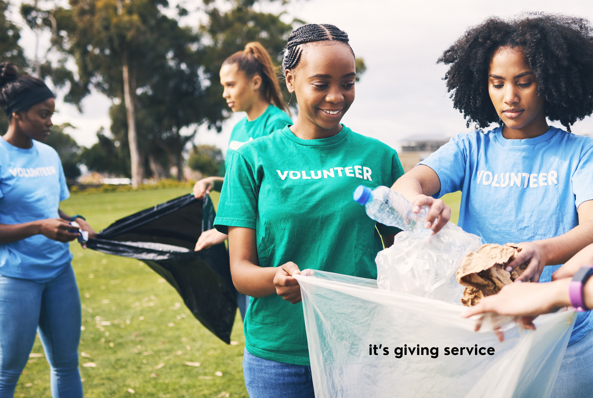 Teen or tween girls with dark skin and black hair wearing volunteer shirts give service by picking up trash at a park.